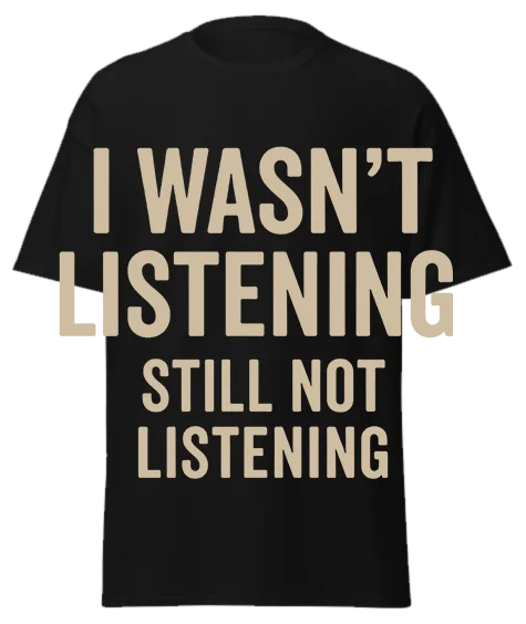 Black unisex t-shirt with off-white text reading "I WASN'T LISTENING STILL NOT LISTENING" – funny sarcastic graphic tee